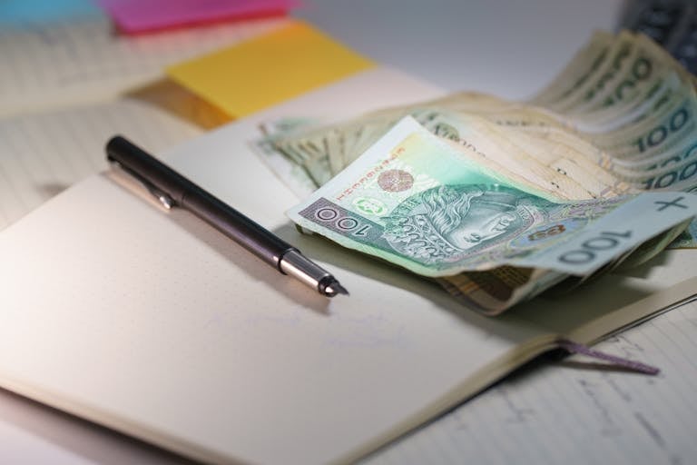 Zbliżenie na banknoty polskich złotych na otwartym notatniku z długopisem, symbolizujące finanse i planowanie budżetu.