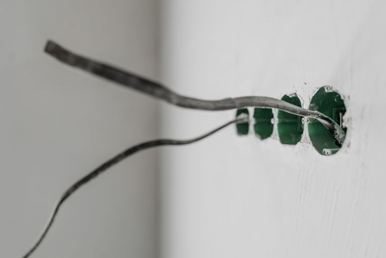 Unfinished electrical outlet installation with exposed wires on a white wall.